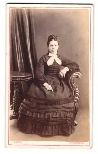 Fotografie G. H. Gibbon, Darlington, junge Dame im schwarzen Kleid mit Überbiss