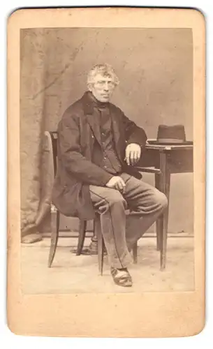 Fotografie August Ducrue, Deggendorf, älterer Herr im Anzug mit Hut auf dem Tisch