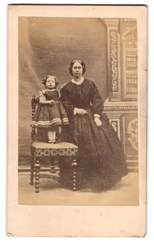 Fotografie unbekannter Fotograf und Ort, Mutter mit ihrer kleinen Tochter auf dem Stuhl im Atelier