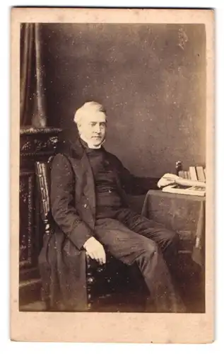 Fotografie Dolamore & Bullock, London, ältere Herr im Anzug posiert lässig sitzend im Atelier