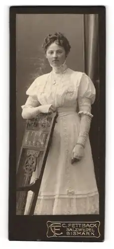 Fotografie C. Fettback, Salzwedel, Portrait junge Dame im weissen Kleid an Stuhl gelehnt