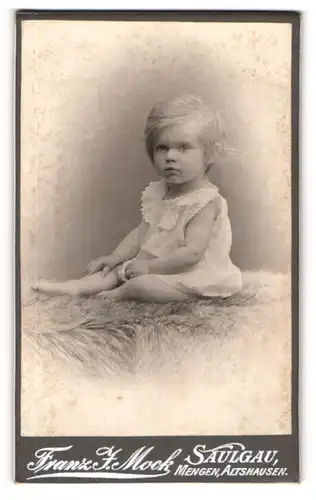 Fotografie Franz J. Mock, Saulgau, Portrait süsses Kleinkind im weissen Hemd auf Fell sitzend