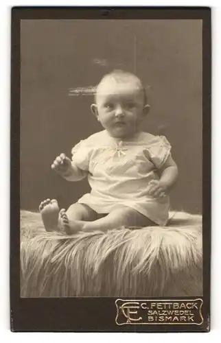 Fotografie C. Fettback, Salzwedel, Portrait süsses Kleinkind im weissen Hemd auf Fell sitzend