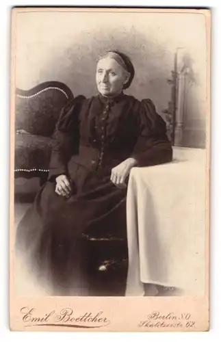 Fotografie Emil Boettcher, Berlin S.O., ältere Frau mit schwarzer Haube sitzend am Tisch