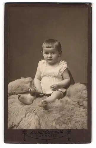 Fotografie Atelier Germania, Chemnitz, Portrait süsses Kleinkind im weissen Hemd mit Rassel auf Fell sitzend