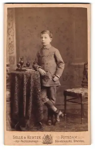 Fotografie Selle & Kuntze, Potsdam, Portrait kleiner Junge in hübscher Kleidung an Tisch gelehnt