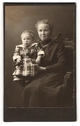 Fotografie H. Flasskämper, Bielefeld, Portrait sitzende Dame im schwarzen Kleid mit Kleinkind auf dem Arm