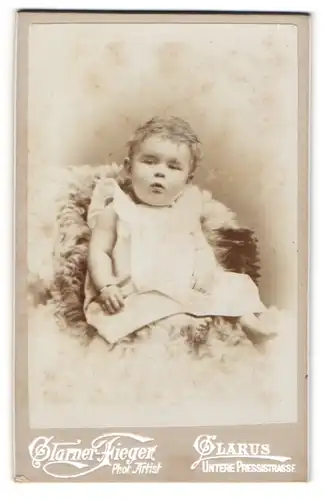 Fotografie Glarner Fieger, Glarus, kleines Kind in weissen Kleid auf Fell sitzend