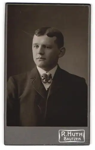 Fotografie R.Huth, Bautzen, Mann in dunklem Anzug mit Rosenfliege