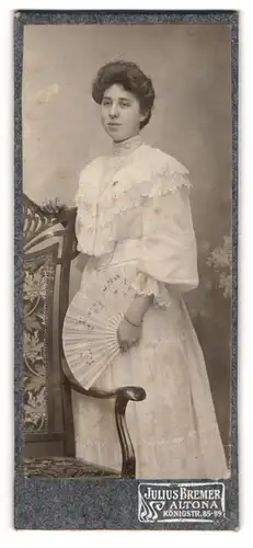 Fotografie Julius Bremer, Hamburg-Altona, Frau mit Fächer und weissem Kleid lehnt an grossen Stuhl