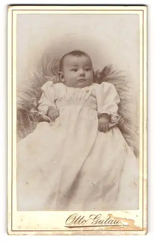 Fotografie Otto Gutau, Berlin-O, Portrait süsses Baby im weissen Kleid auf Fell sitzend