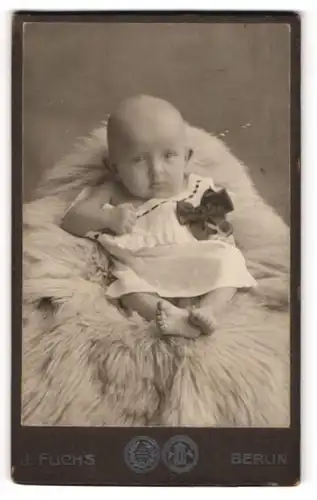 Fotografie J. Fuchs, Berlin, Portrait süsses Baby im weissen Hemd auf Fell sitzend