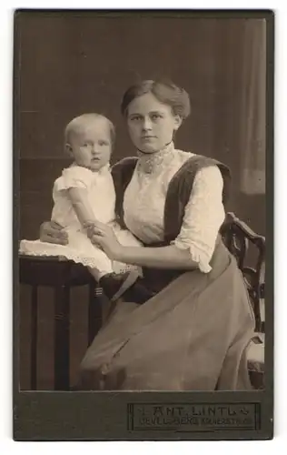 Fotografie Ant. Lintl, Gevelsberg, Portrait bürgerliche Dame mit Kleinkind im Arm am Tisch sitzend