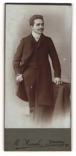 Fotografie M. Hirsch, Berlin-Spandau, Portrait elegant gekleideter Herr an Tisch gelehnt