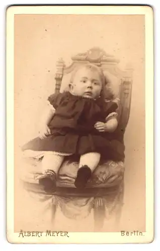 Fotografie Albert Meyer, Berlin, Kleinkind in schwarzem Kleidchen sitzt auf einem gepolstertem Stuhl