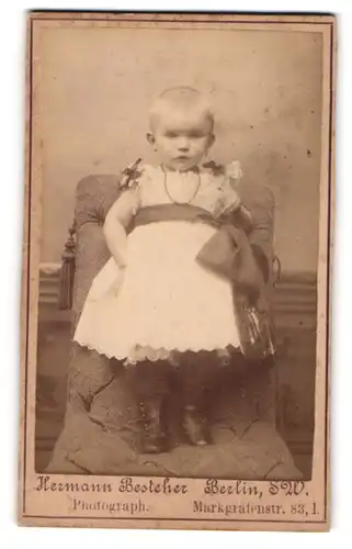 Fotografie Hermann Besteher, Berlin, Kleinkind in weissem Kleid steht auf Sessel