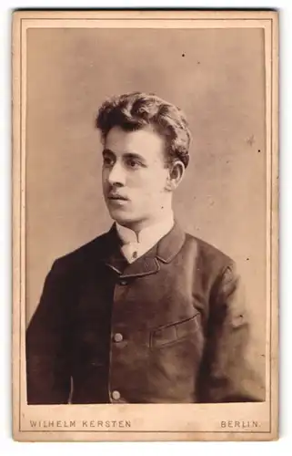Fotografie Wilhelm Kersten, Berlin, Junger Mann mit gelocktem Haar trägt weisses Hemd und dunklen Mantel