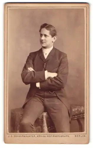 Fotografie J. C. Schaarwächter, Berlin, Portrait modisch gekleideter Herr mit verschränkten Armen auf Tisch sitzend