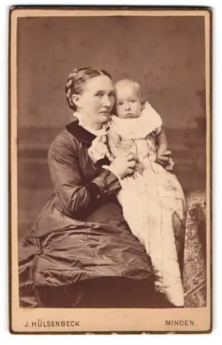 Fotografie J. Hülsenbeck, Minden, Portrait sitzende Dame im festlichen Kleid mit Baby auf dem Arm