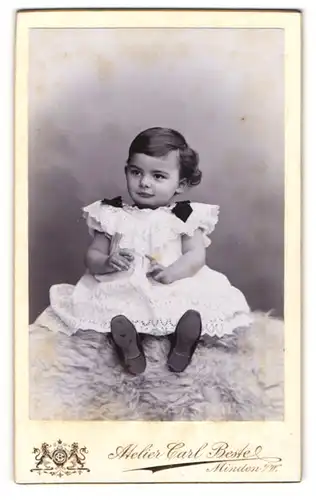 Fotografie Carl Beste, Minden, Portrait süsses Kleinkind im weissen Kleid auf Fell sitzend