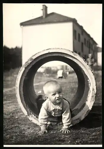 Fotografie unbekannter Fotograf und Ort, niedliches Kleinkind krabbelt durch eine Betonrohr in einem Neubaugebiet