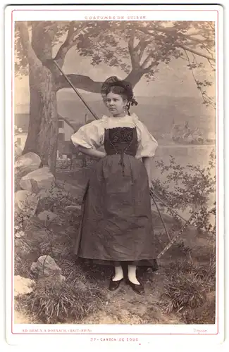 Fotografie Ad. Braun, Dornach, schöne junge Dame im Trachtenkleid aus Zug mit Rechen vor einer Studiokulisse