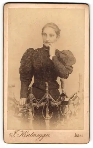 Fotografie J. Hinteregger, Ischl, Junge Dame in schwarzem taillierten Kleid mit leichtem Lächeln und dunklen Haaren