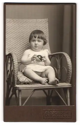 Fotografie E. Swoboda, Vöcklabruck, Portrait süsses Kleinkind im weissen Hemd mit Ball auf Kissen sitzend