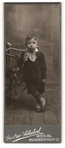 Fotografie Gustav Schubert, Berlin, Breitenseerstrasse 22, Kleiner Junge im Anzug mit Zierschleife in lässsiger Haltung