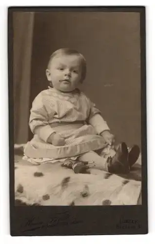 Fotografie Herm. Feldt, Lübeck, Breitestr. 31, Niedliches Kleinkind im gestreiften Kleid mit Spielzeugpferd