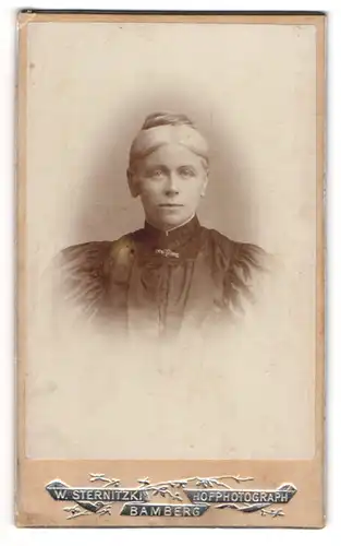 Fotografie W. Sternitzki, Bamberg, Hainstr. 2, Junge blonde Dame in schwarzem Kleid mit silberner Brosche