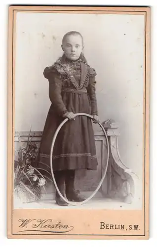Fotografie W. Kersten, Berlin, Krausenstr. 35, Junges Mädchen im dunklen Kleid mit gelangweiltem Blick und Reifen