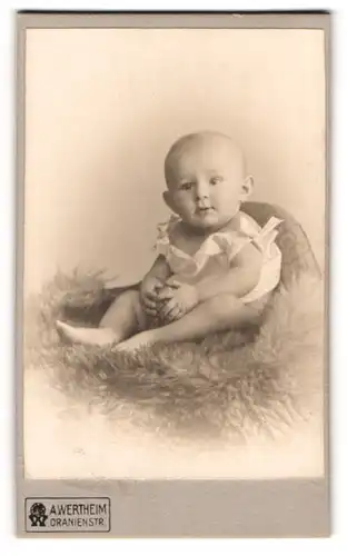 Fotografie A. Wertheim, Berlin, Portrait süsses Kleinkind im weissen Hemd mit Ball auf Fell sitzend