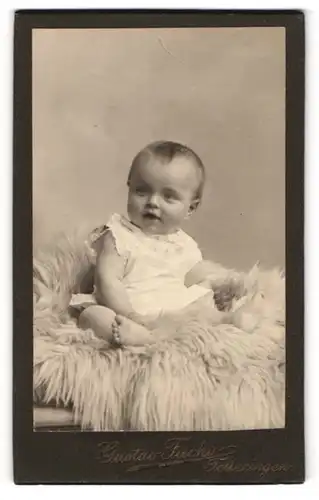 Fotografie Gustav Fuchs, Felleringen, lachendes süsses Baby auf einem Fell sitzend