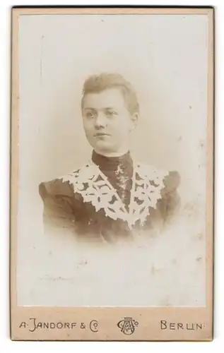 Fotografie A. Jandorf, Berlin, Frau in dekorativen dunklem Kleid mit weissen Blumenakzenten