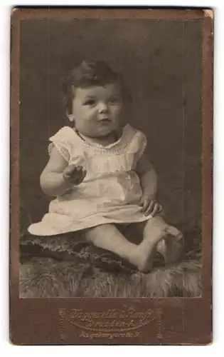 Fotografie Taggeselle & Ranft, Dresden-A., Portrait niedliches kleines Mädchen im weissen Kleidchen auf Fell sitzend