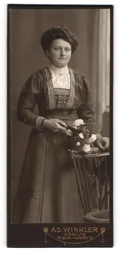 Fotografie Ad. Winkler, Görlitz, Portrait hübsch gekleidete Dame mit Blumen an Stuhl gelehnt