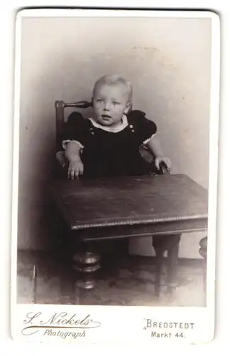 Fotografie S. Nickels, Bredstedt, Portrait kleines Mädchen im modischen Kleid am Tisch sitzend