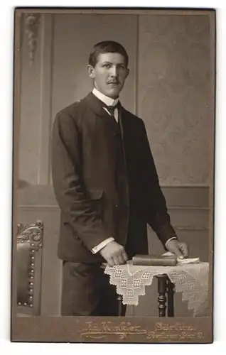 Fotografie Ad. Winkler, Görlitz, Portrait stattlicher Herr im Anzug mit Krawatte an Tisch gelehnt