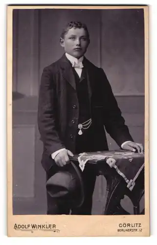 Fotografie Adolf Winkler, Görlitz, Portrait junger Mann im Anzug mit Fliege und Hut in der Hand