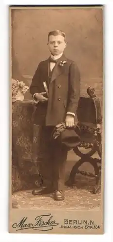 Fotografie Max Fischer, Berlin, junger Knabe im Anzug mit Hut und Bibel zur Konfirmation