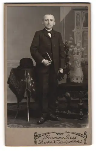 Fotografie Hermann Gross, Dresden, junger Knabe im dunklen Anzug mit Bibel und Melone auf dem Tisch, Konfirmation