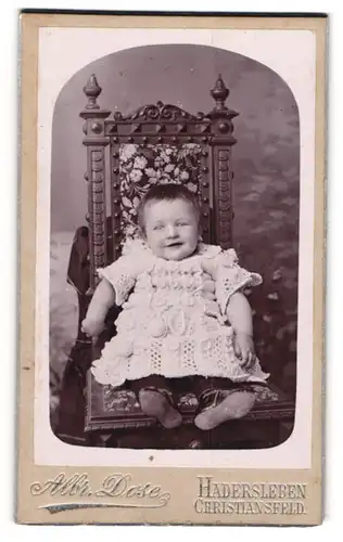 Fotografie Albr. Dose, Hadersleben, Niedliches Baby in weissem Kleid sitzt lachend auf einem Stuhl