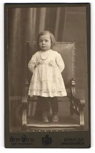 Fotografie Otto Witte, Berlin, Skalitzerstr. 54, Niedliches kleines Mädchen im weissen Kleid mit Perlenkette schaut brav
