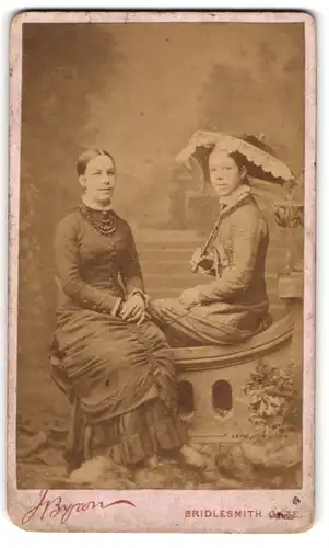 Fotografie J. Byron, Nottingham, zwei junge Engländerinnen in Biedermeierkleidern mit Schirm, Studiokulisse