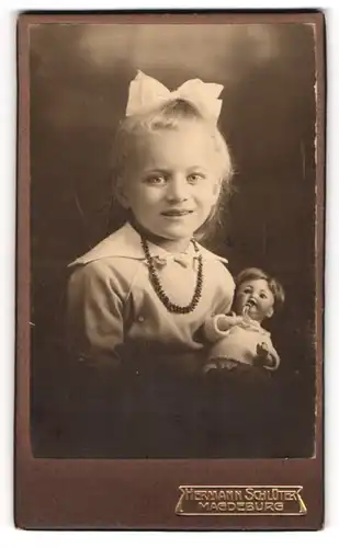 Fotografie Hermann Schlüter, Magdeburg, niedliches Mädchen mit ihrer Puppe im Arm, Haarschleife