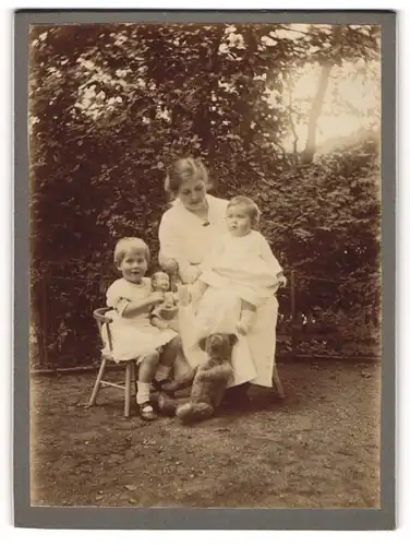 Fotografie unbekannter Fotograf und Ort, Mutter mit ihren beiden Kindern samt Teddybär und Puppe