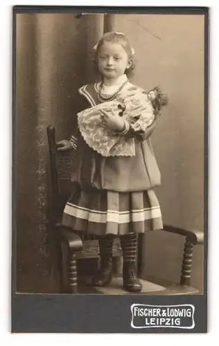 Fotografie Fischer & Ludwig, Leipzig, kleines Mädchen mit ihrer Puppe im Arm auf einem Stuhl stehend