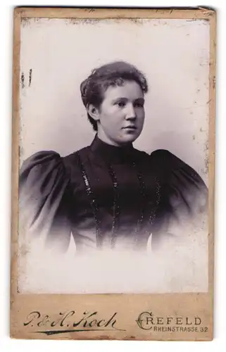 Fotografie P. & H. Koch, Crefeld, Portrait junge Dame im schwarzen Kleid mit Puffärmeln