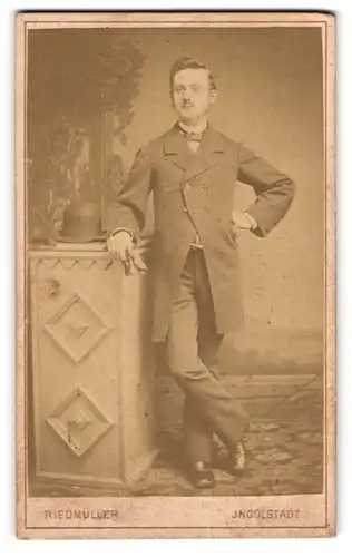 Fotografie N. Riedmüller, Ingolstadt, Portrait modisch gekleideter Herr mit Melone an Sockel gelehnt